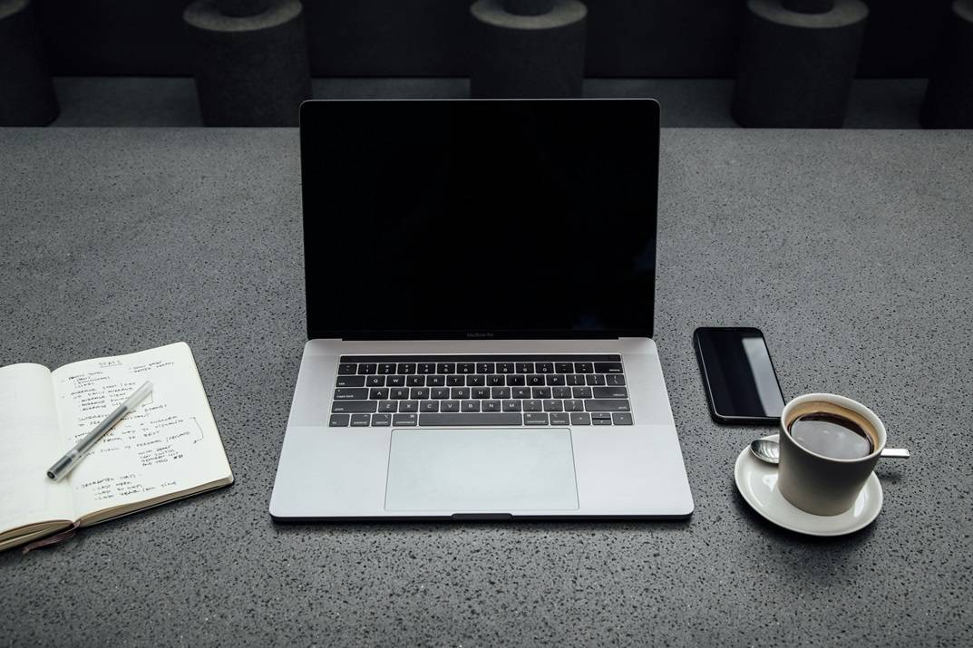 Laptop, open notebook, phone, and cup of coffee on gray table