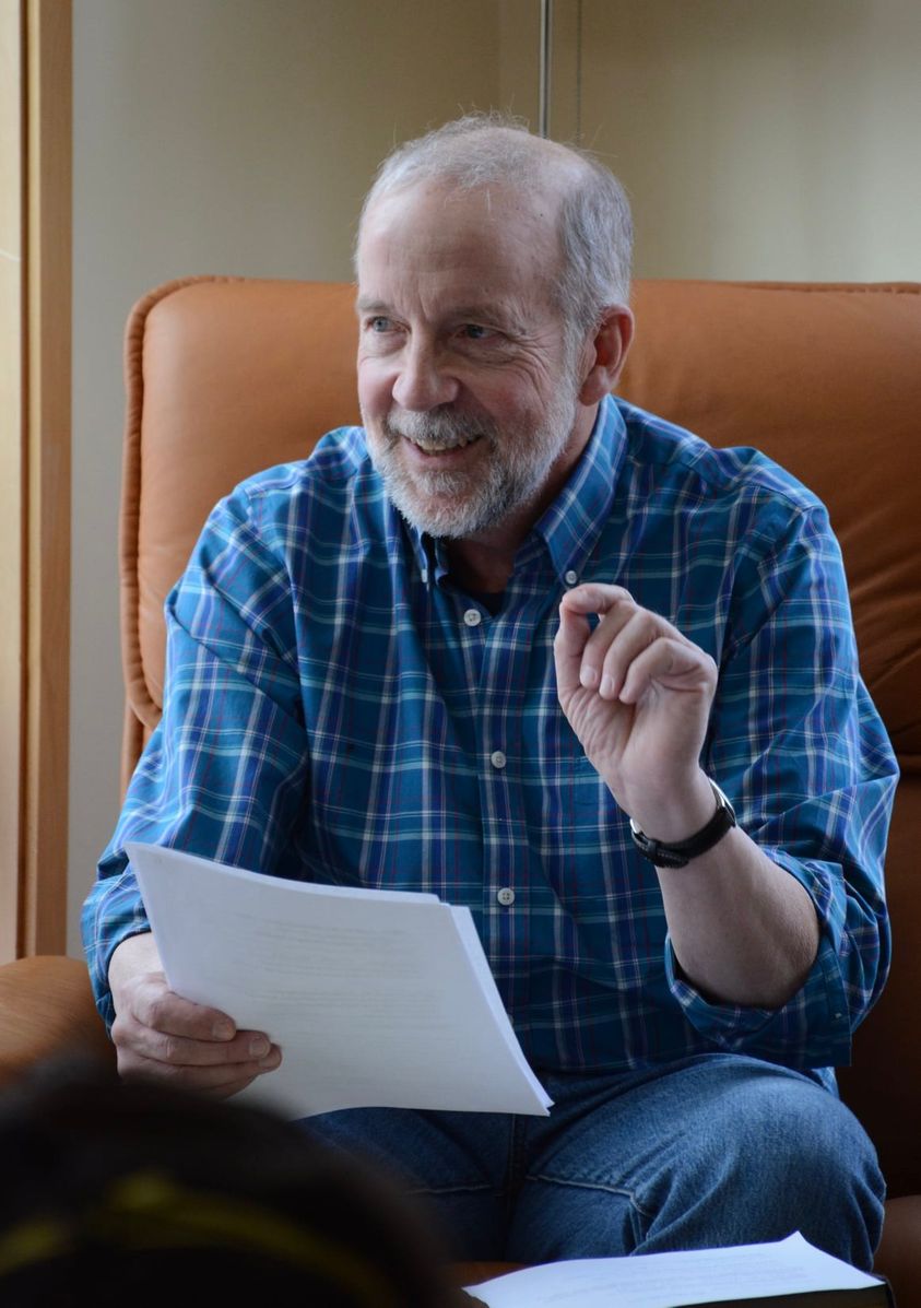 Tom Kizzia seated, holding papers and smiling.