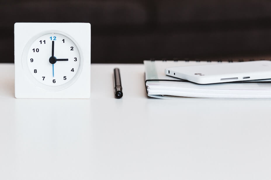 Clock, pen, planner, and cell phone on white desk