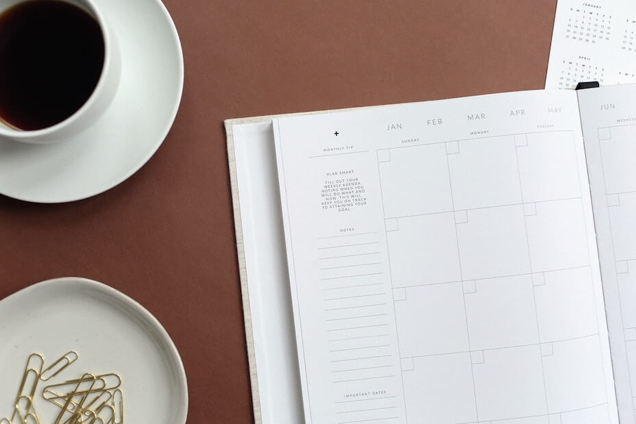 Open planner, cup of coffee, small tray of gold paperclips on desk surface