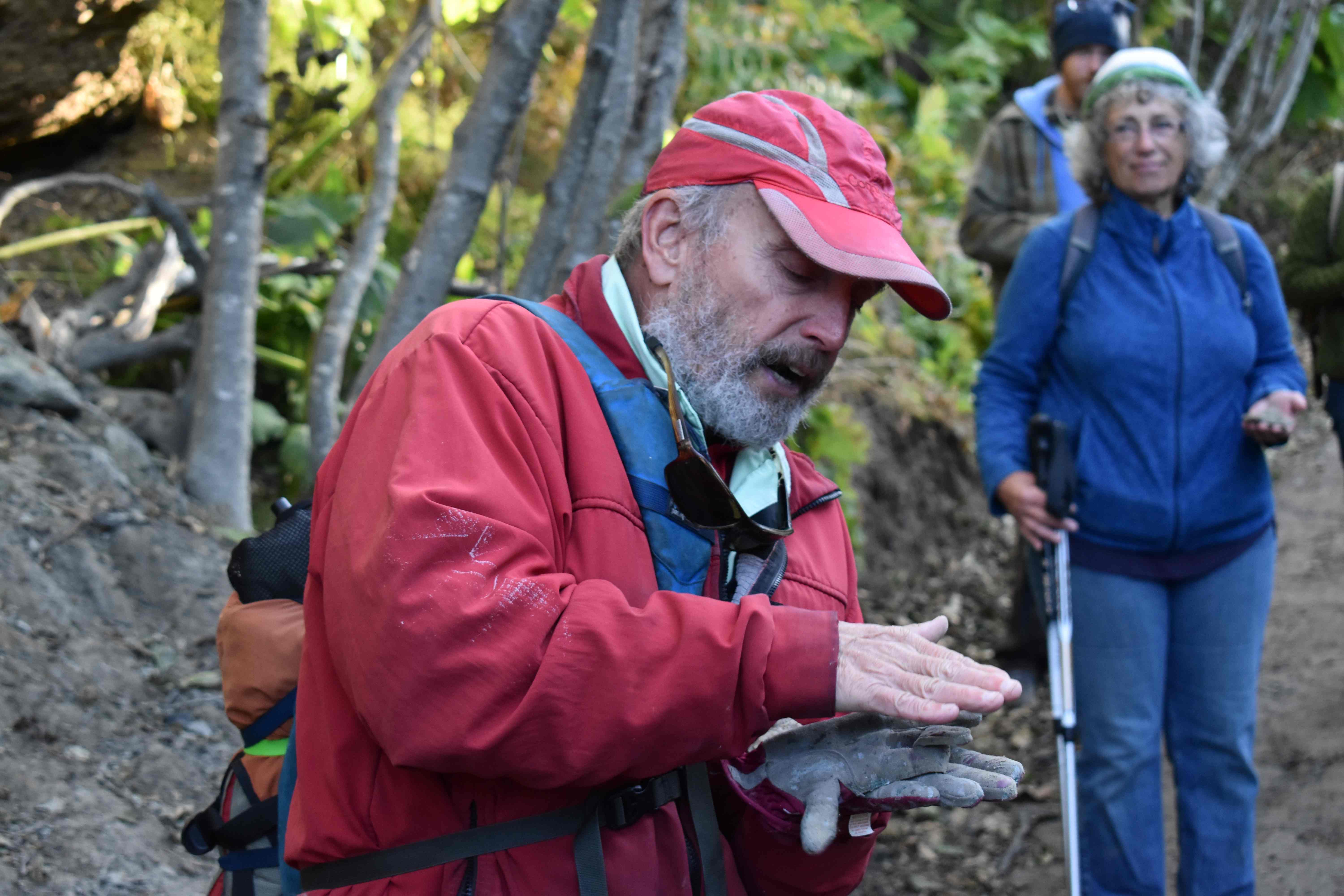 Taz Tally holding a rock on the wooded trail with students watching.