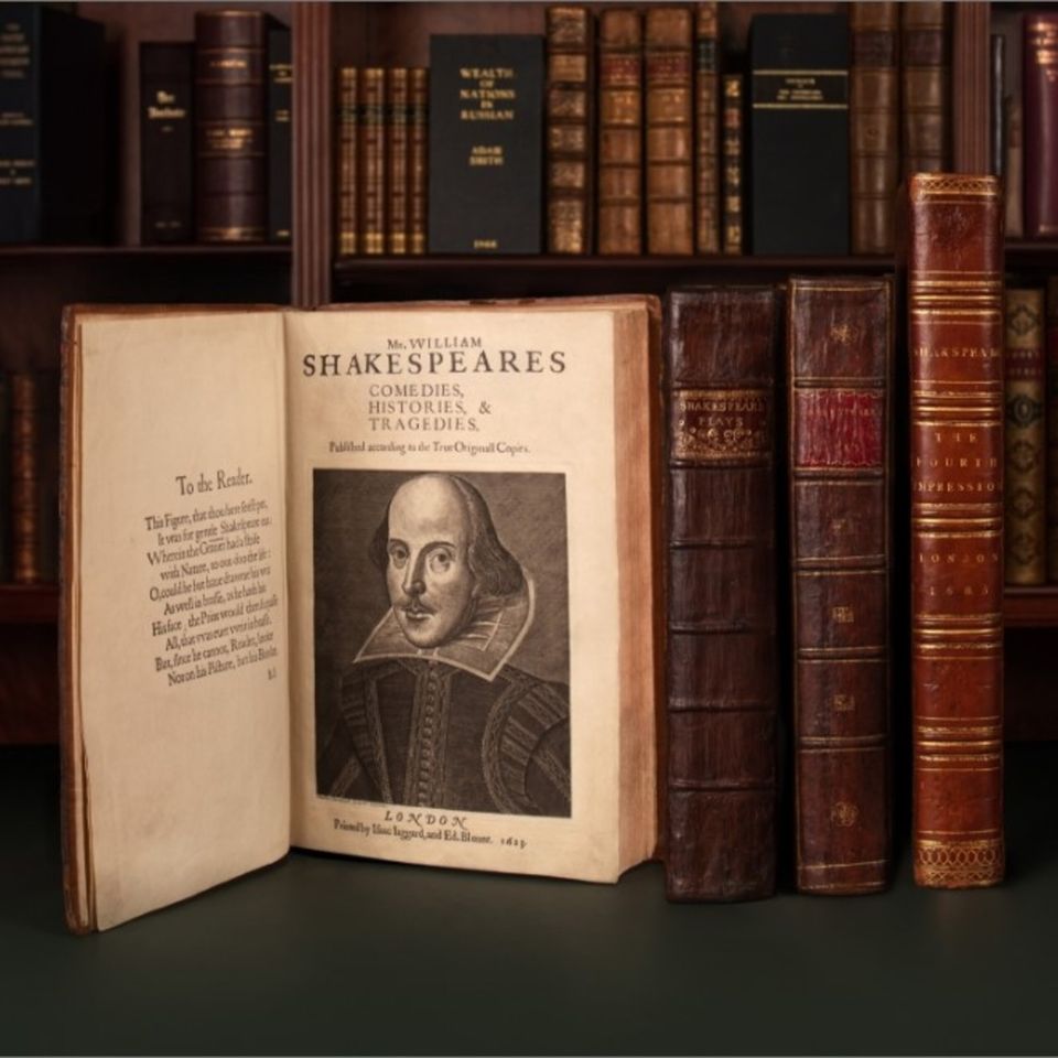 shelves of old books with one opened to a volume of Shakespeares works