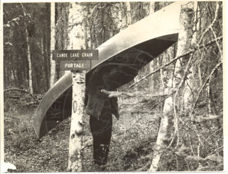 Will Troyer carrying his canoe at the first Swan Lake canoe system portage, Kenai Peninsula late 1960's