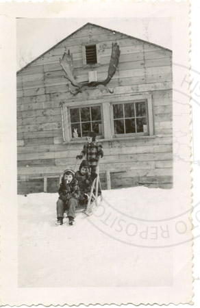 Laurie Lancashire, Karen Lee, and Jocele Faa on a sled in front of one of the Faa family's buildings, Soldotna 1951