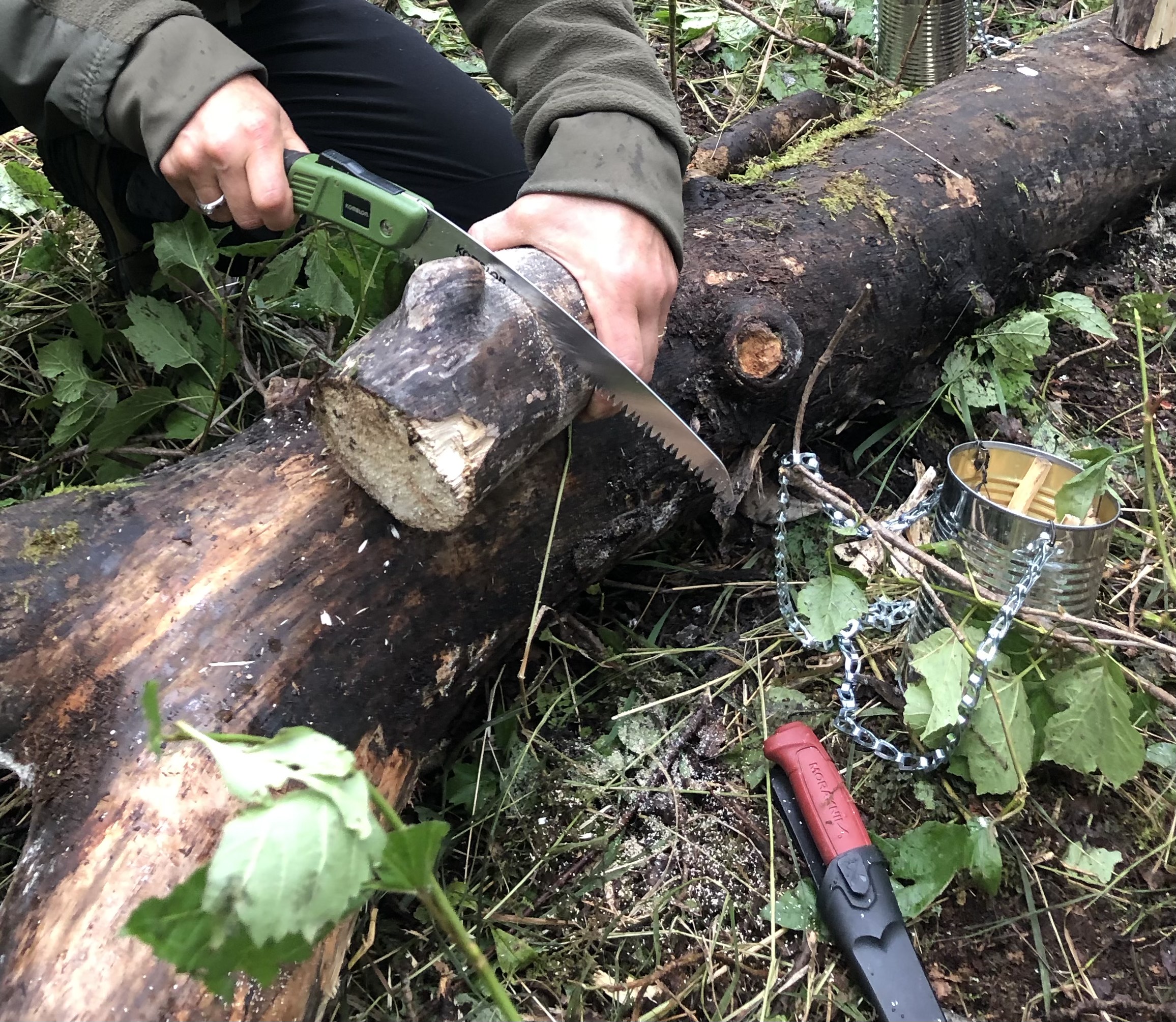 Person sawing a log with a small handsaw 