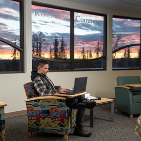 Young man in plaid shirt working on laptop in colorful chair with sunrise in background