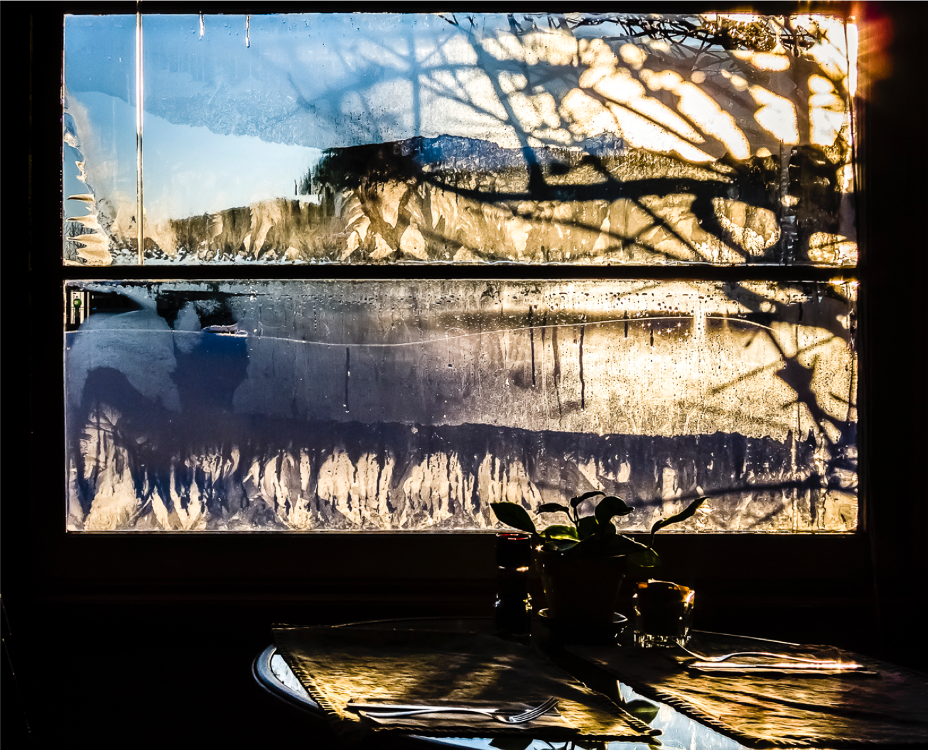 A small table set for two next to a grosted window with the shadows of trees refecting against the glass and ice